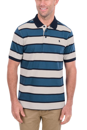 The man is wearing the Thomas Cook Martin Polo, a short-sleeve, collared men’s polo made from soft cotton pique with blue, navy, and beige horizontal stripes. He pairs it with khaki pants and smiles against a plain white background.