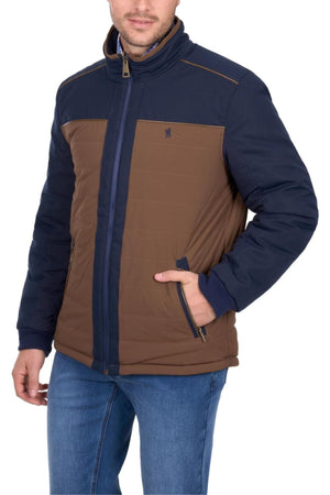 A man wears the Thomas Cook Toby Reversible Jacket in brown and navy blue, featuring a high collar, side pockets, and a small chest logo, paired with blue jeans. His face is partially visible.