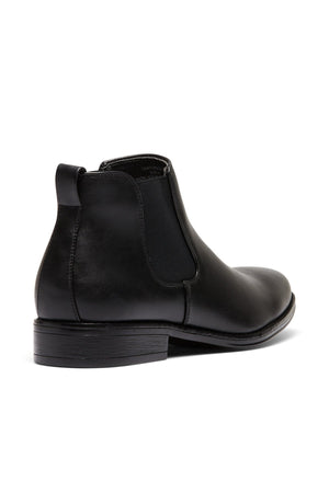 The UNcut Canterbury Boot is a durable black leather Chelsea boot with elastic side gussets, a pull tab at the back, and a low stacked heel, shown from a rear side angle on a white background.