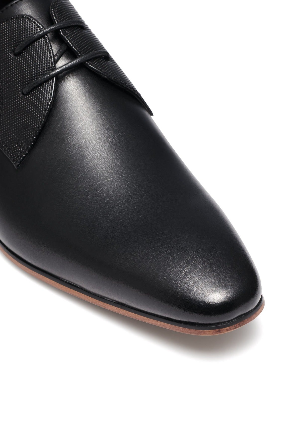 Close-up of the UNcut Chartwell Shoe in sleek black leather, featuring a pointed toe ideal for formal occasions. It has an embossed upper panel, textured fabric near the laces, and a thin light brown sole, resulting in a design that's effortlessly modern and polished.