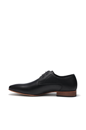 The UNcut Chartwell Shoe is a sleek black leather dress shoe with a pointed toe, brown wooden heel, and black laces. Its smooth finish and embossed upper panel make it perfect for formal events, elegantly showcased from a side profile against a plain white background.