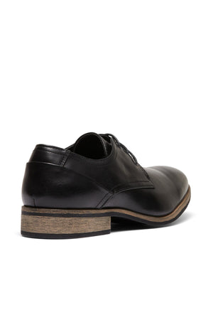 The UNcut Rhine Shoe is shown in black with a non-leather upper and low wooden heel, viewed from the rear side on a white background. Featuring laces and a polished finish, it's ideal for formal occasions.