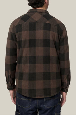 A person stands with their back to the camera, wearing the Hard Yakka Legends Sherpa with FREE Beanie—featuring a brown and black plaid flannel design, fleece body lining, and dark jeans against a plain light background.