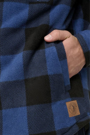 A close-up shows a hand in the pocket of a blue and black plaid Hard Yakka Legends Sherpa with FREE Beanie, featuring a brown circular logo patch near the hem and thermal insulation for extra warmth.