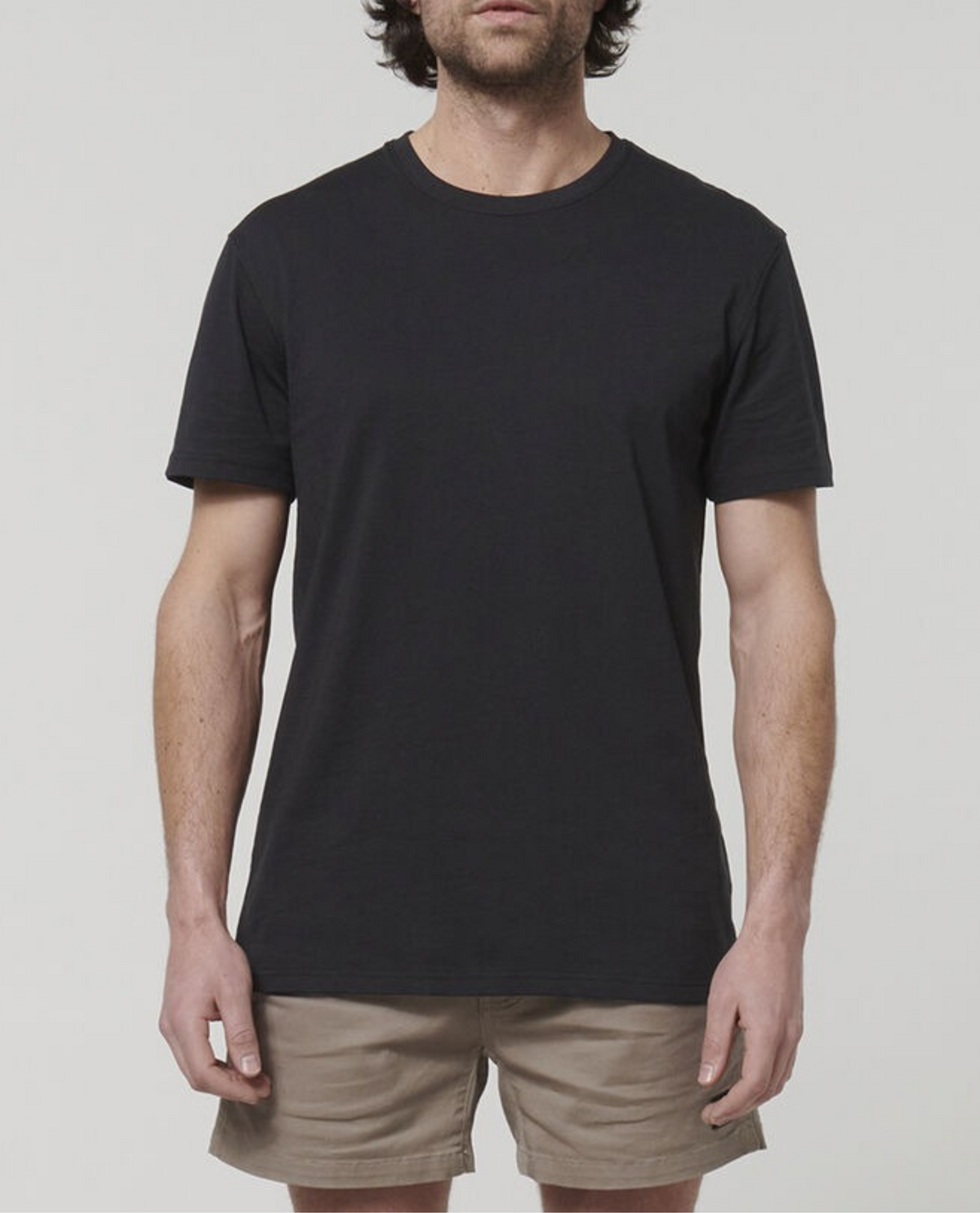 A person wearing a Black Hard Yakka Core Tee, made from Australian Cotton, and beige shorts stands against a plain white background. The person's face is not visible.