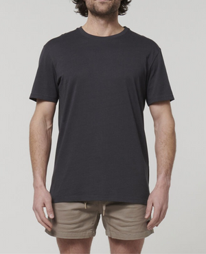A man with medium-length hair stands in a neutral pose, wearing a plain charcoal Hard Yakka Core Tee and beige shorts made from 100% Australian Cotton. The background is a light grey color. His face is not visible, as the photo is cropped at his shoulders.