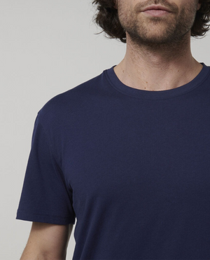 A man wearing a Hard Yakka Core Tee in plain navy blue, made from 100% Australian cotton, is shown from the shoulders up against a neutral background. The image captures part of his face but emphasizes the t-shirt's premium quality which originates from Australian cotton farms.