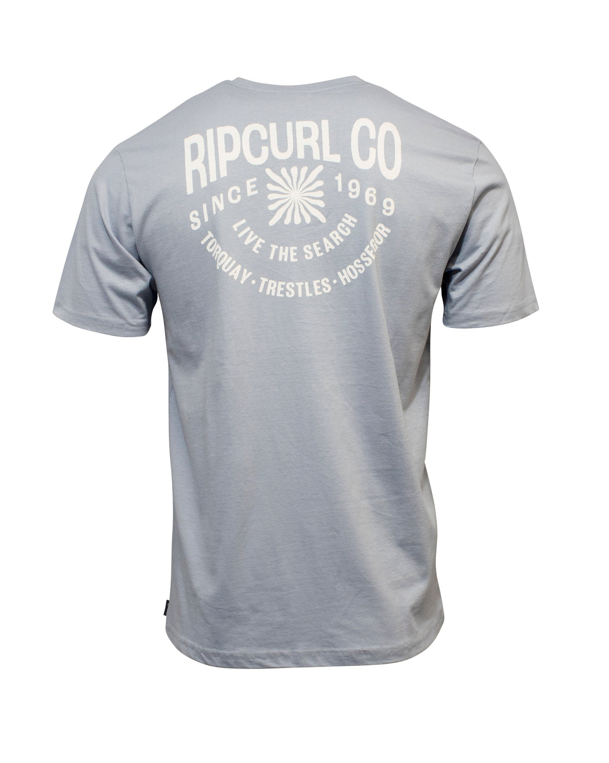 The Rip Curl Cosmic Burst Tee is a light blue 100% cotton shirt, shown from the back with bold white "RIP CURL CO SINCE 1969 LIVE THE SEARCH" text, small location names, and a sunburst graphic for a comfortable casual style.