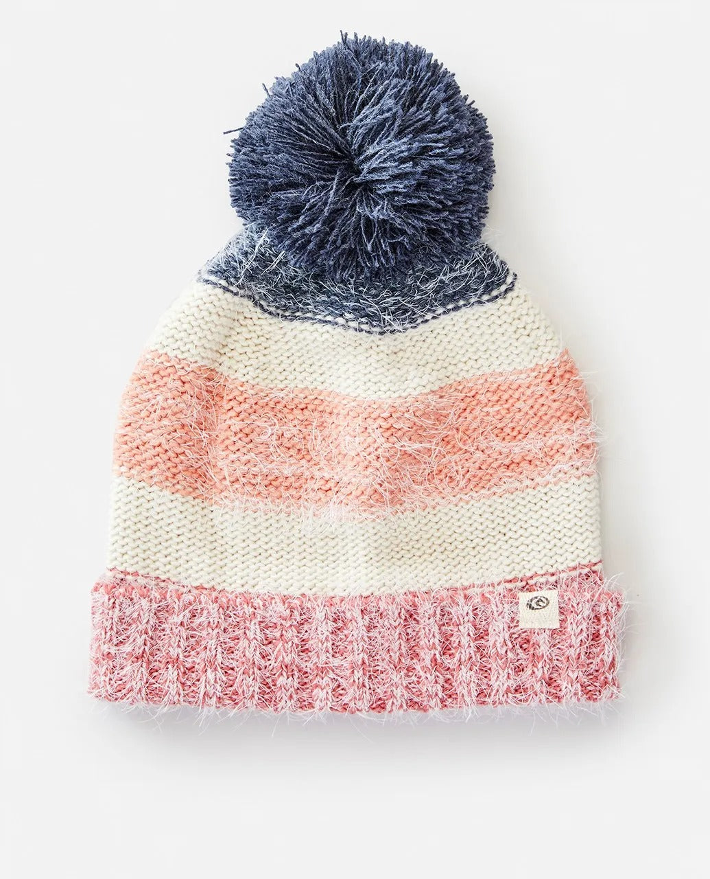 The Rip Curl Surf Tree House Pom Pom Beanie is a chic winter accessory with pink, white, and blue stripes. It features a large blue pom-pom on top and a small logo patch near the brim. The knit combines fluffy and smooth yarns for stylish texture this season.