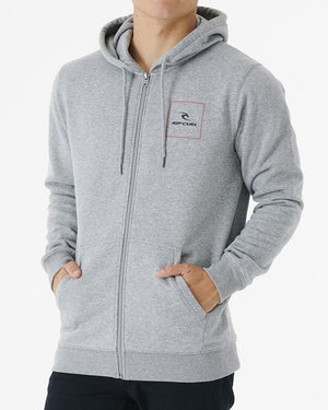 Wearing the Rip Curl Corp Icon Zip Thru, a person stands against a white background. This gray hoodie, featuring a small logo on the chest, drawstrings, and a front zipper, combines comfort and style as they rest their hands in the front pockets.