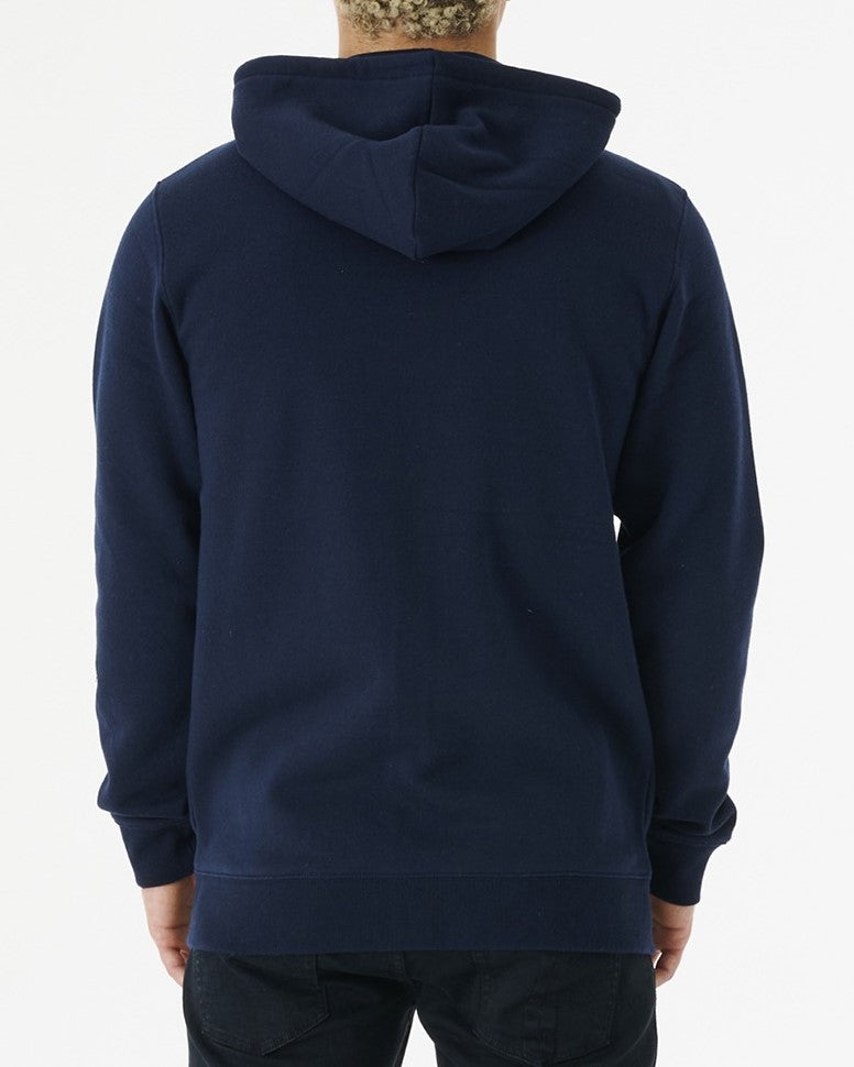 A person is seen from the rear, wearing a dark blue Rip Curl Corp Icon Zip Thru hoodie with soft fleece lining and black pants, standing against a plain white backdrop.