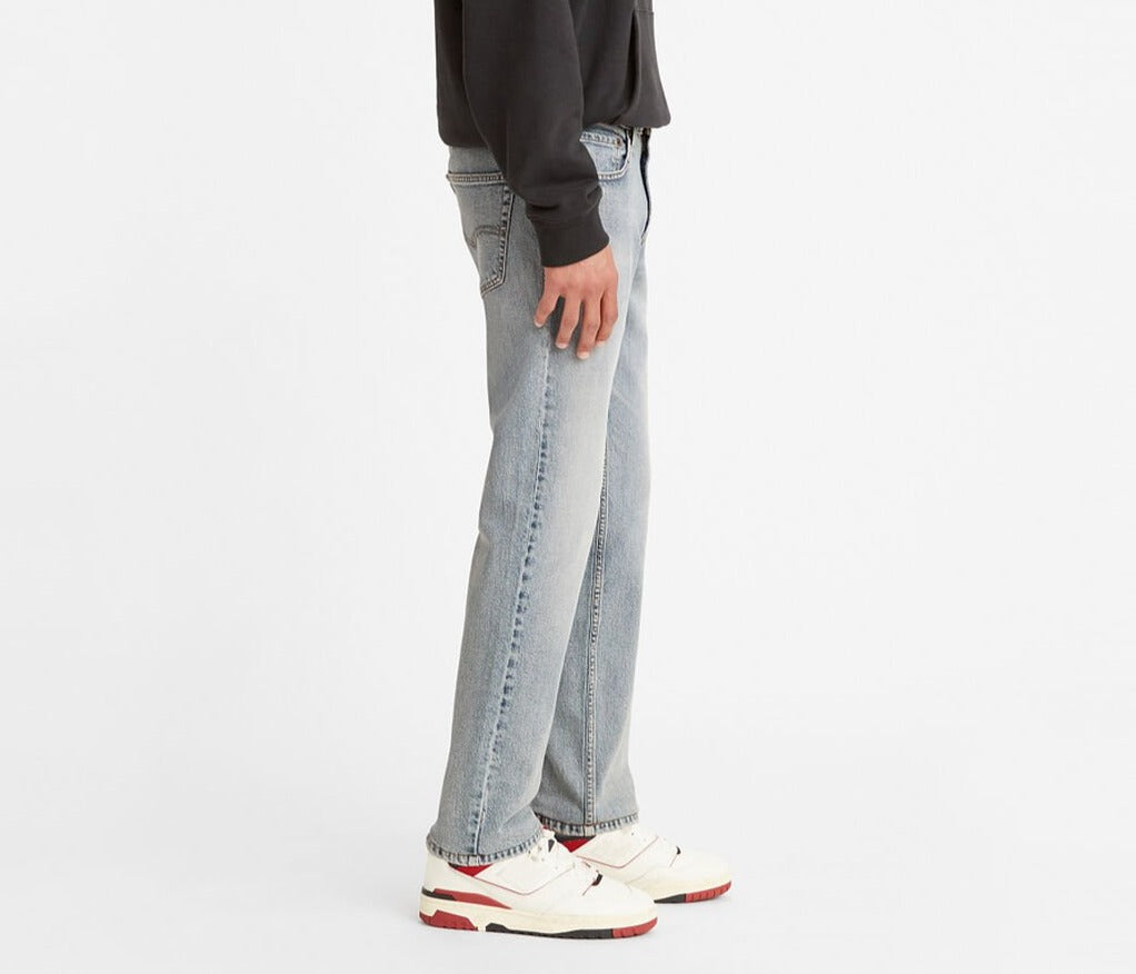 A person wearing stylish Levis 511 Slim Jean in light blue, a black hoodie, and white sneakers with red accents stands sideways against a plain white background.