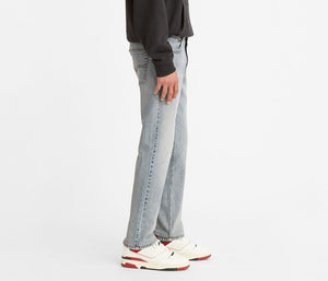 A person wearing stylish Levis 511 Slim Jean in light blue, a black hoodie, and white sneakers with red accents stands sideways against a plain white background.