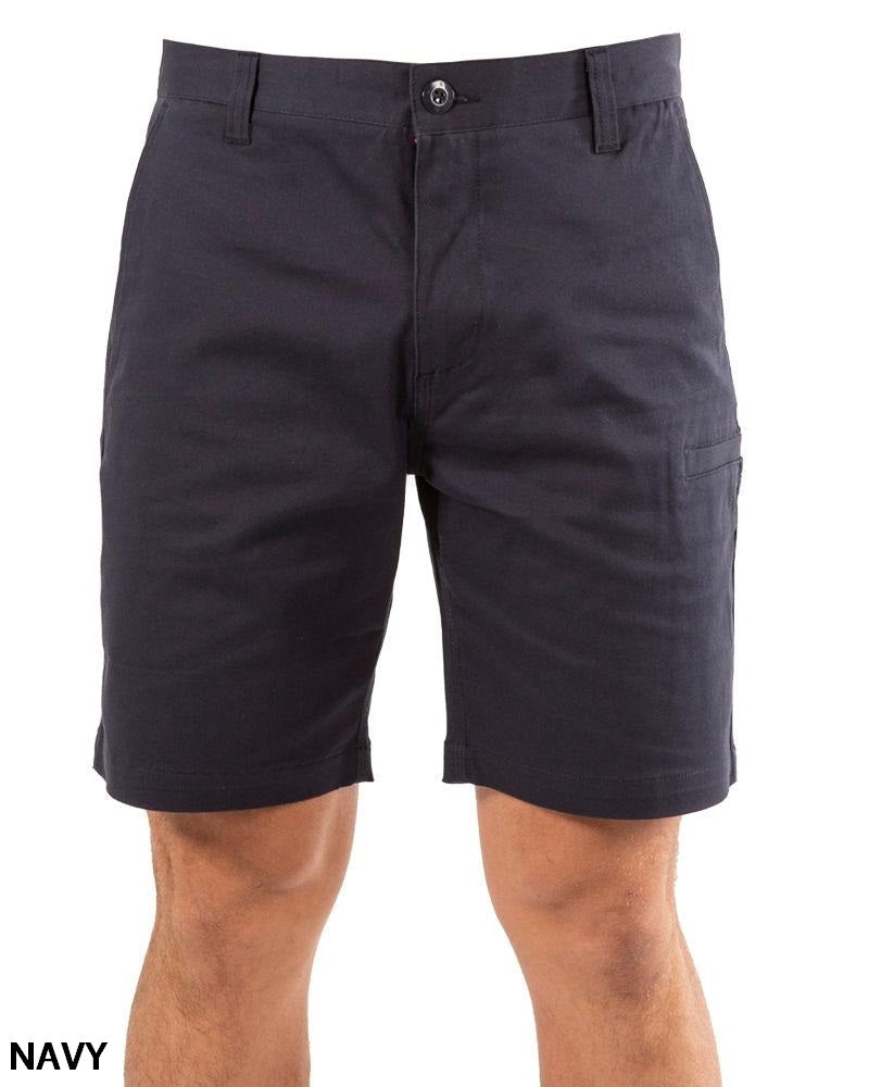 A person wears UNIT Ignition Stretch Shortβknee-length, navy blue work shorts made from durable stretch fabric with button and zipper closure, front and side pockets. "NAVY" appears in the bottom left corner.