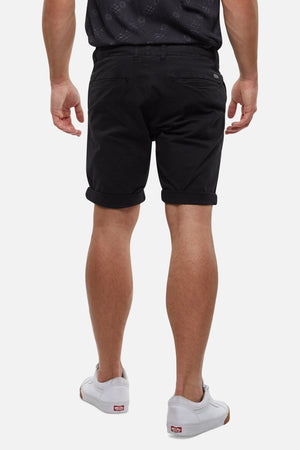 A person is seen from the back, wearing a black shirt, comfortable Industrie The Rinse Short, and white sneakers. The background is plain white.