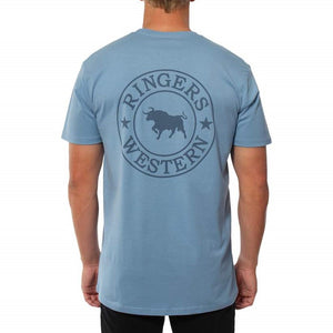 A person wearing a light blue Ringers Western Signature Bull Original Fit T-Shirt with a circular design featuring a bull on the back. The individual, dressed in black pants and facing away from the camera, showcases this comfortable 100% cotton tee.