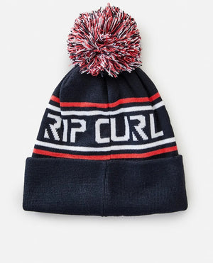 The Rip Curl Fade Out Tall Beanie, made of acrylic, showcases a vibrant red, white, and navy pom-pom on top. It features stylish red and white stripes with "RIP CURL" prominently displayed in bold white lettering across the front.