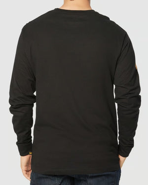 A person in a black CAT Trademark Banner Long Sleeve Tee paired with jeans stands back to the camera against a plain backdrop.