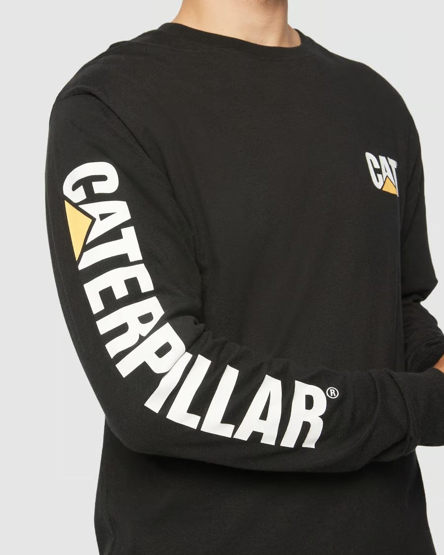 A person is wearing a CAT Trademark Banner Long Sleeve Tee made of 100% cotton. "CATERPILLAR" is in white on the right sleeve, and "CAT" with a yellow triangle logo appears on the chest. The person's face is not visible.