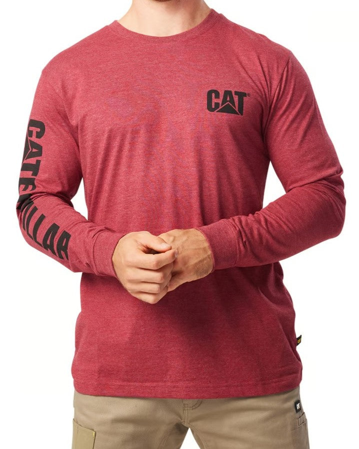 A person is wearing a comfortable, red CAT Trademark Banner Long Sleeve Tee, showcasing the "CAT" logo on the chest and "CATERPILLAR" on the sleeve. They pair it with beige pants while standing against a plain background.