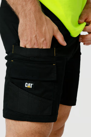 Close-up of a person wearing black CAT Elite Operator Shorts, which feature multiple utility pockets and a "CAT" logo patch on one of the pockets. The individual is also sporting a bright yellow shirt, tucked into the shorts with elastic inserts. Only the midsection and upper thighs are visible.