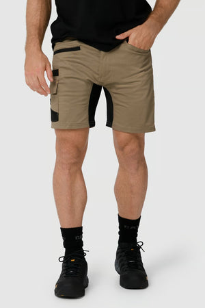 A person wearing a black T-shirt, CAT Elite Operator Short in khaki with black detailing and utility pockets, black socks, and black shoes stands with one hand in their pocket against a plain light gray background.