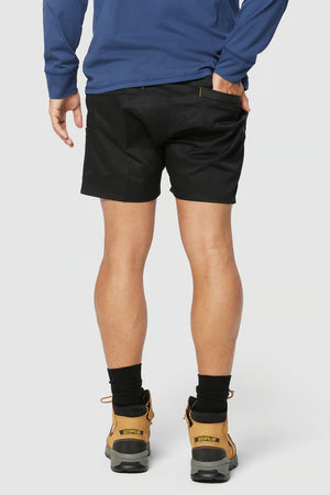 Back view of a person wearing a long-sleeve blue shirt, black CAT Short Haul Shorts with an elastic waist, black socks, and tan hiking boots. The person is standing with hands in their back pockets against a plain white background.