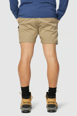 Revised Sentence: Rear view of a person wearing a blue long-sleeve shirt, CAT Short Haul Shorts in tan with an elastic waist and a cargo pocket, black socks, and brown work boots. The person is standing with their legs slightly apart against a plain, light background.