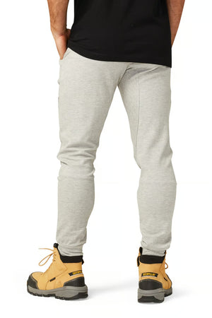 Someone in CAT Track Pant and sturdy tan work boots with black soles is standing, hands in pockets, facing away against a plain white background.