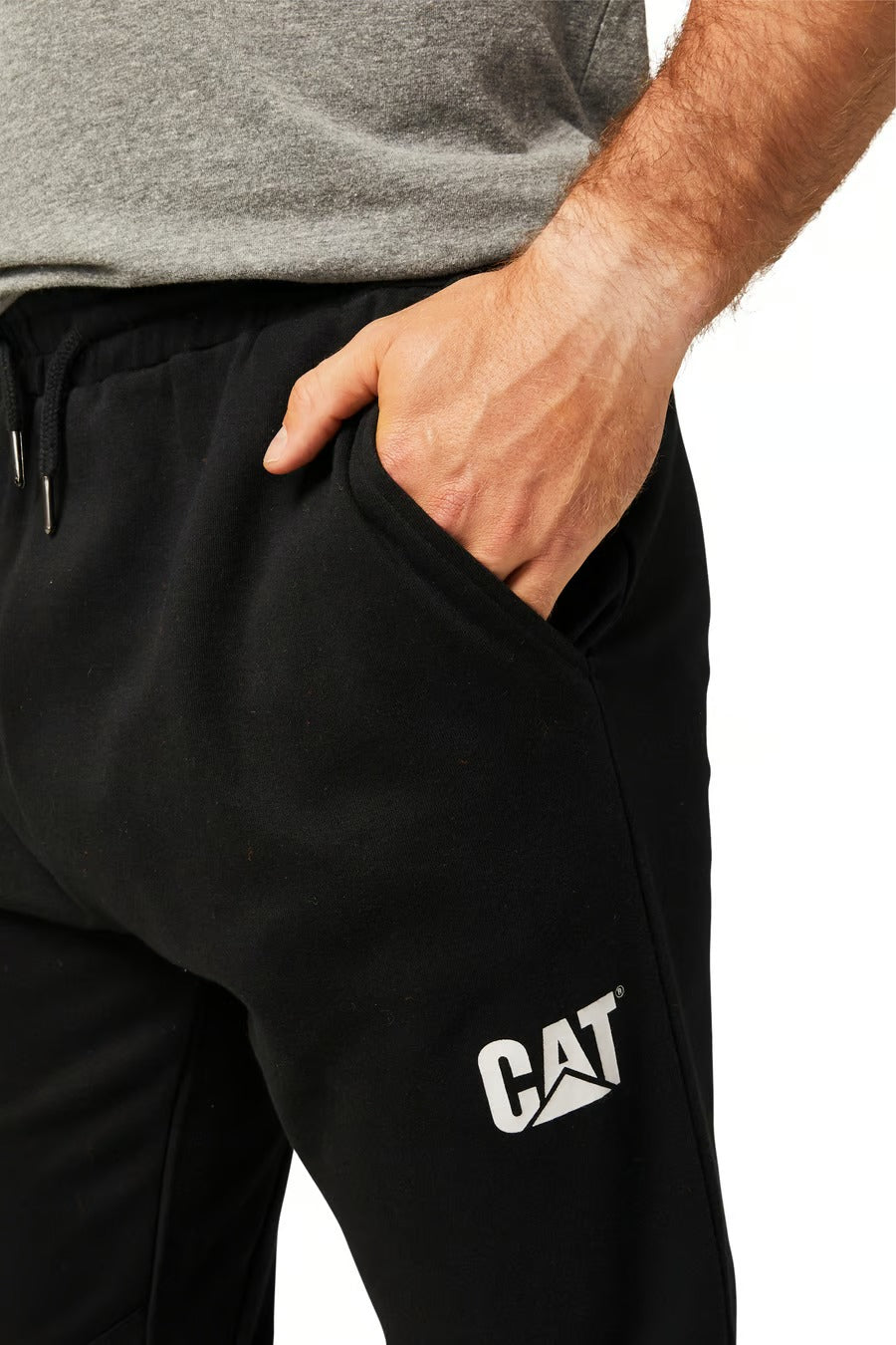 A person is shown from the waist down, dressed in CAT Track Pants. The black jogger pants include a "CAT" logo on the upper thigh, and the person's right hand rests in the pocket. They are also wearing a gray shirt against a white background.