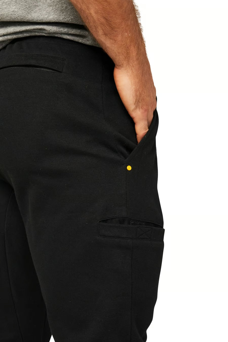 A person wearing the black CAT Track Pant with their right hand placed in the pocket. They are also wearing a gray top, and the image focuses on the CAT Track Pant's durable side view.