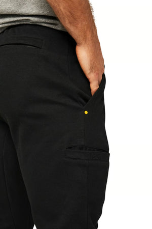 A person wearing the black CAT Track Pant with their right hand placed in the pocket. They are also wearing a gray top, and the image focuses on the CAT Track Pant's durable side view.