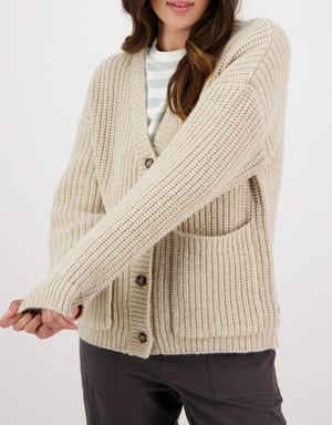 A person wearing the Swanndri Braunton Knit Cardigan with large buttons over a white and light gray striped shirt and dark pants, posing with arms slightly crossed.
