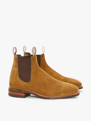 The RM Williams Comfort Suede Craftsman Boot is a pair of caramel-colored suede leather Chelsea boots with dark brown elastic side panels. These handcrafted Australian boots feature loop pulls on both the back and front for easy wear and removal, and they are equipped with wooden soles and dark brown comfort rubber outsoles. The background is plain white.