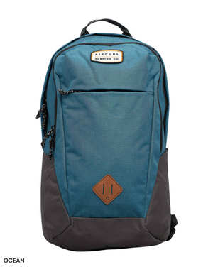 The Rip Curl Overtime 30L Driven Backpack is blue and black, made from recycled polyester, and features a front zip pocket and a brown diamond-shaped patch with the brand logo at the top, offering an eco-friendly and stylish choice for your adventures.