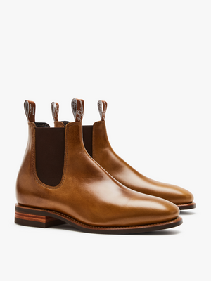 The RM Williams Comfort Craftsman Boot is a pair of tan pull-up leather Chelsea boots, handmade in Adelaide with elastic side panels, back pull tabs, and stacked wooden heels, shown on a white background.