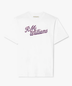 The RM Williams Script T-Shirt is a white cotton t-shirt with "R.M. Williams" printed in cursive purple letters on the front. It features short sleeves, a crew neck, and stylish logo branding.