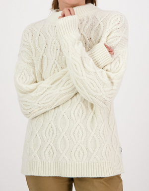 A person wearing the Swanndri Pendeen Cable Neck Crew, a cream-colored jumper with long sleeves and a chunky knit design, paired with khaki pants. The background is plain white.