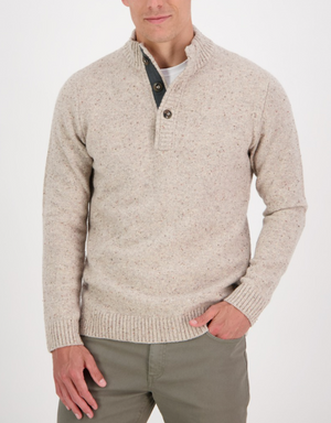 A man wears the Swanndri Clifton Half Placket Knit, a light beige speckled jumper with a buttoned collar, paired with khaki pants. He stands against a white background with one hand in his pocket and his face partially visible.
