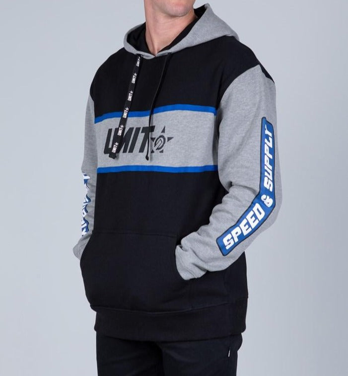 A person wears the UNIT Zenith Hoodie Fleece in black and gray with blue stripes, a "UNIT" logo on the chest, "SPEED & SUPPLY" on the sleeves, and keeps their hands in its comfy kangaroo pocket.