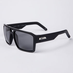The UNIT Vault Polarised Eyewear is a pair of black sunglasses with thick square frames and dark-tinted polycarbonate polarized lenses. The temples feature a metal plate with the brand name "UNIT" and an arrow symbol. Offering UV protection, the lightweight frame ensures comfort, while the inner side of the temples reads "SEE NO LIMITS.