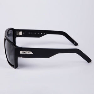 Introducing the UNIT Vault Polarised Eyewear: a sleek pair of black sunglasses with "SEE NO LIMITS" inscribed on the inside arms. These stylish sunglasses feature polycarbonate polarized lenses that offer UV protection and a lightweight frame for comfort. The modern design is highlighted by a silver logo and detailing on the arms, while the dark rectangular lenses strikingly contrast against any background.