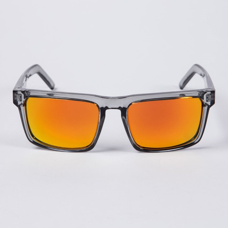 The UNIT Primer Polarised Eyewear is a pair of stylish sunglasses featuring transparent gray frames and reflective orange lenses, displayed on a white background. The contemporary design boasts rectangular lens shapes and sleek, lightweight arms, offering both UV protection and modern flair.
