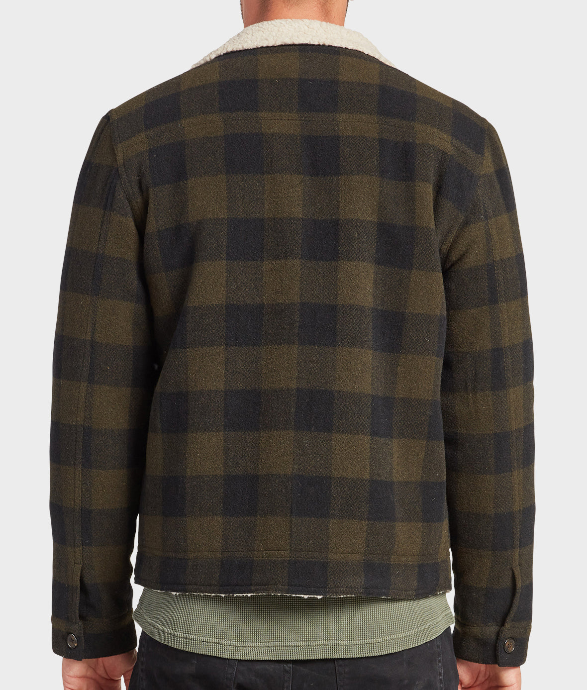 A person is shown from the back wearing the Academy Brand Davie Jacket, featuring green and black plaid, a cream sherpa collar, paired with dark pants and a green ribbed shirt.