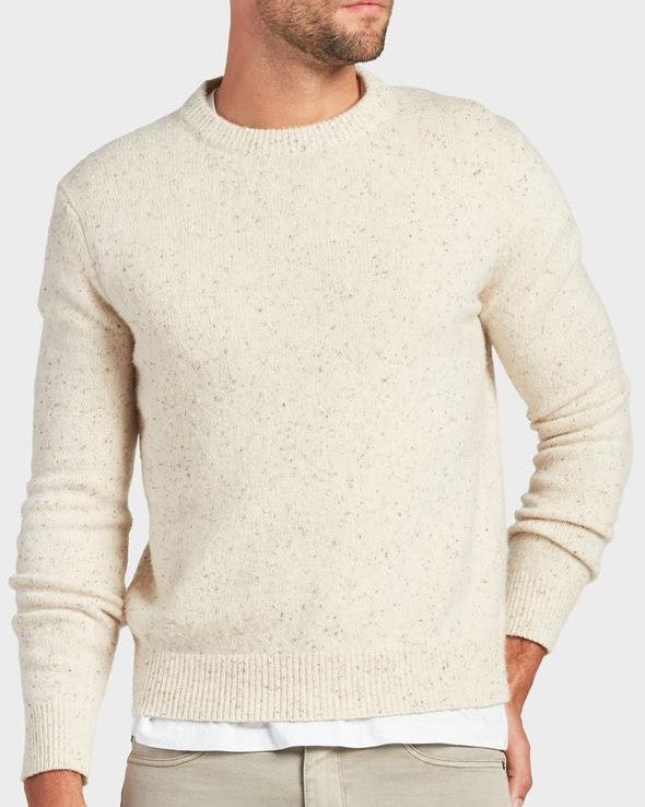 A man wearing the Academy Brand Shoreditch Crew Knit in cream speckle over a white shirt and light beige pants stands with one hand in his pocket against a plain background.