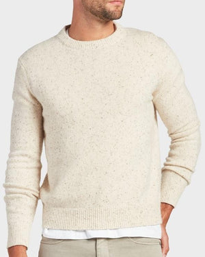 A man wearing the Academy Brand Shoreditch Crew Knit in cream speckle over a white shirt and light beige pants stands with one hand in his pocket against a plain background.