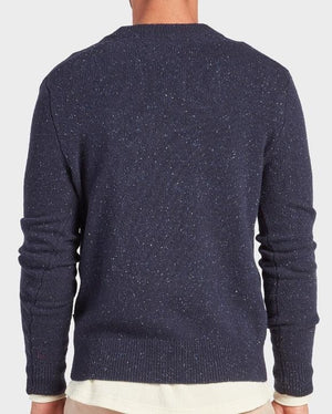 A person is shown from the back wearing the Academy Brand Shoreditch Crew Knit, a dark blue speckled lambswool jumper, over a white shirt and beige pants against a plain light background.