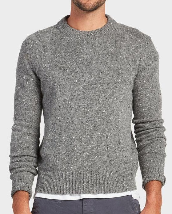 A man wears the Academy Brand Shoreditch Crew Knit in grey over a white shirt with dark pants, standing against a plain light background. His head is partially out of frame.