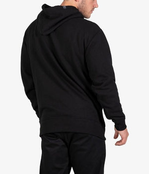Wearing the UNIT Stride Fleece Hoodie and black pants, a person stands with their back to the camera and head turned slightly, the minimalist style emphasized by a plain, light background.