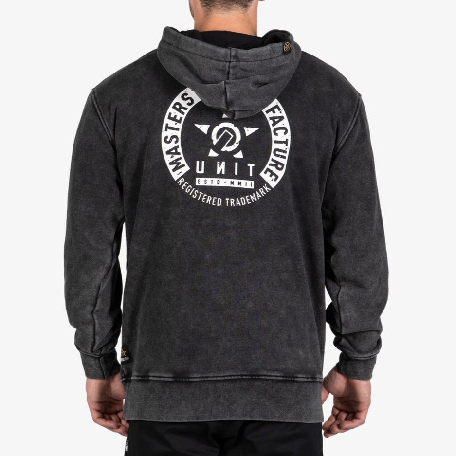A man is seen from behind wearing the UNIT Branch Fleece Hoodie in black acid-wash, featuring a large white circular logo with "UNIT," "REGISTERED TRADEMARK," and "MASTERS OF MANUFACTURE" text.